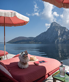 Christof Wagner Liegen und rosa Sonnenschirme direkt am Traunsee mit Blick auf den Traunstein.