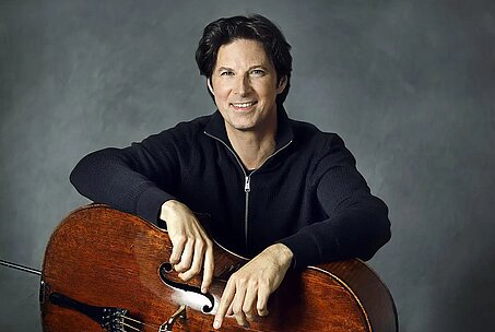 © Uwe Arens Daniel Müller-Schott sitzt mit seinem Cello vor einem dunklen Hintergrund.