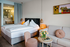 Modernes Hotelzimmer mit Doppelbett, Sofa und offenem Badbereich, stilvolle Minisuite am Traunsee